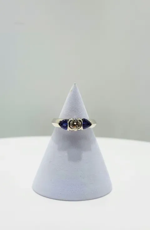 Silver ring with a dark blue stone displayed on a gray cone stand against a light background