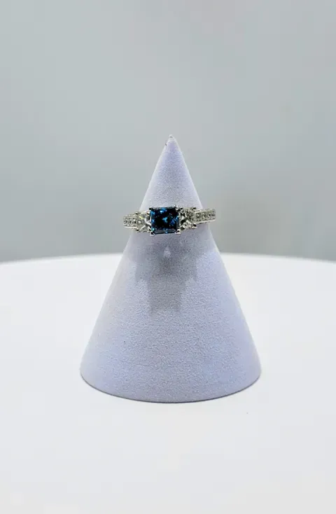 White cone jewelry display with a gold ring set with a blue gemstone, centered on a white table.