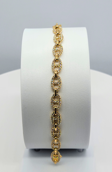 Gold bracelet with ornate links displayed vertically on a white cylindrical stand.