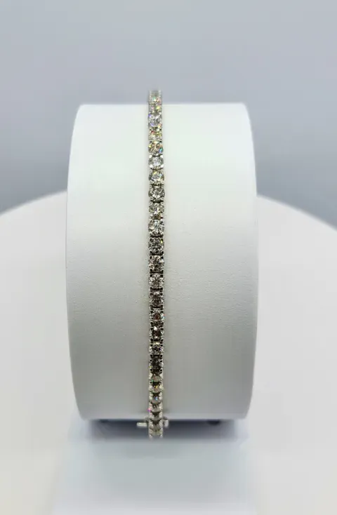 Delicate gold and crystal bracelet displayed upright on a white cylindrical stand.
