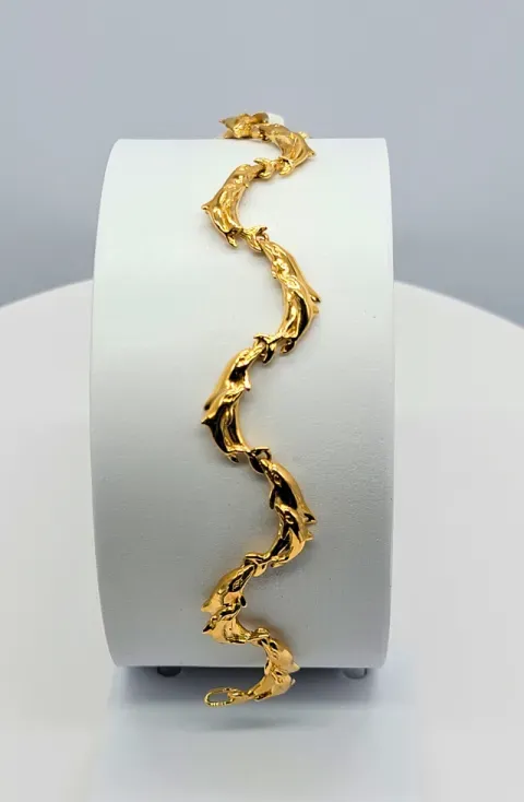 Gold zigzag bracelet displayed on a white cylindrical stand against a gray background
