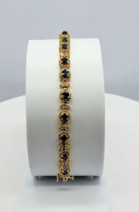 Gold bracelet with dark blue stones displayed on a white cylindrical stand