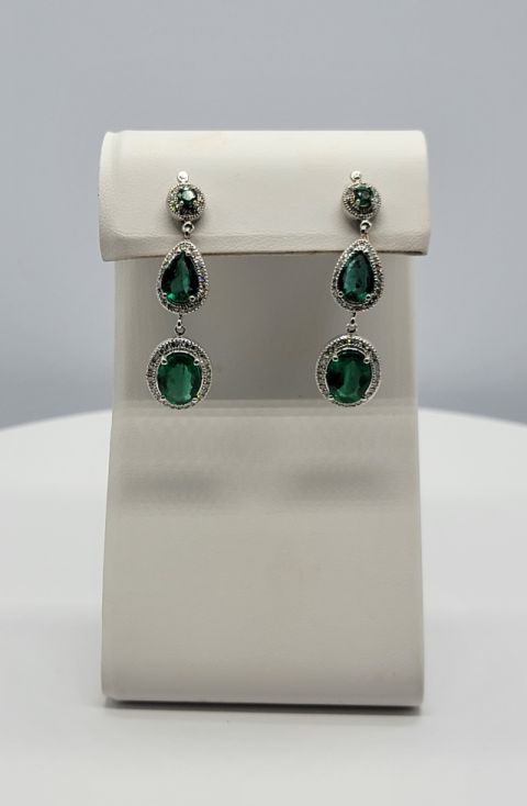 Silver drop earrings with green gemstones displayed on a white stand