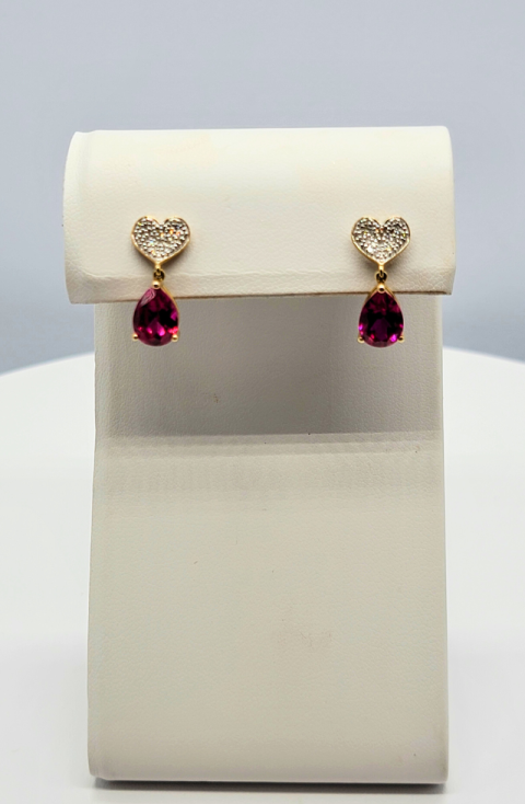 Pair of gold heart-shaped earrings with pink gemstones on a white display stand