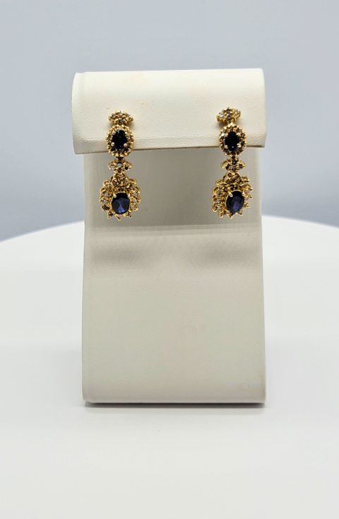 Pair of gold drop earrings with blue stones displayed on a white stand