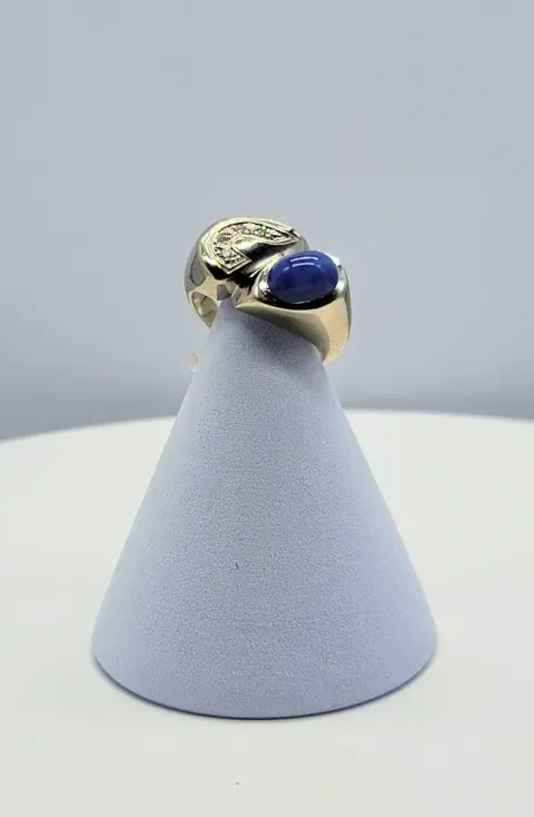 Gold ring with blue and silver stones displayed on a gray cone stand