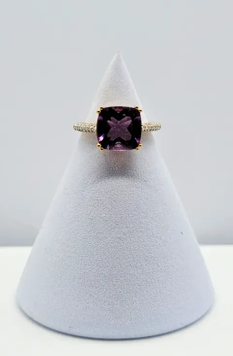 Gold ring with a purple gemstone on a white display cone