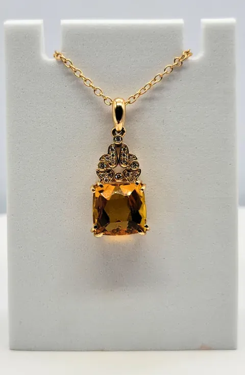 Gold pendant necklace with a large amber gemstone on a white display stand