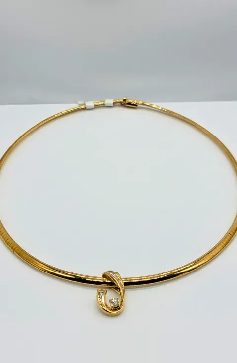 Gold necklace with a black accent and a small pendant on a light background