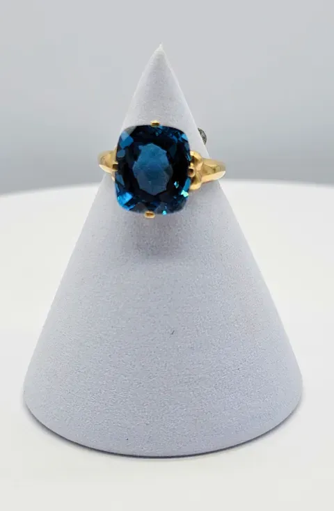 Blue gemstone ring with gold setting displayed on a white cone stand