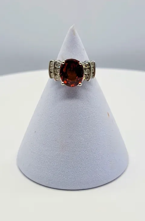 Silver ring with an oval dark red gemstone displayed on a white cone stand.