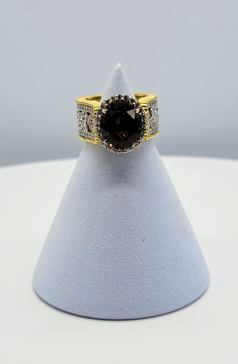 Gold ring with a large dark gemstone displayed on a light gray cone stand.