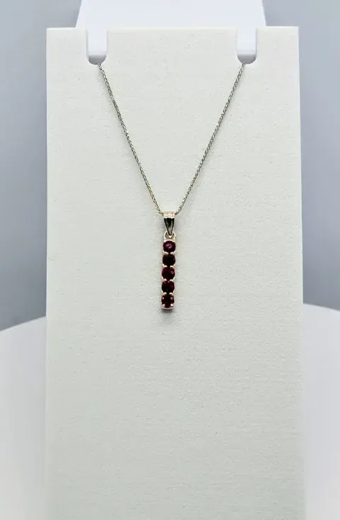 Silver necklace with a vertical row of red gemstones on a white display bust