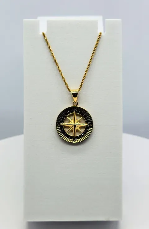 Gold pendant necklace with a black-and-gold compass medallion on a white display stand