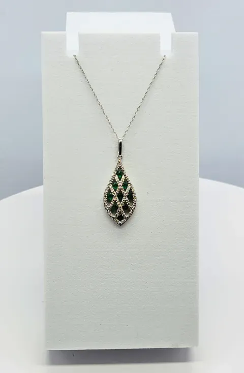 Teardrop green gemstone pendant on a silver necklace displayed on a white stand
