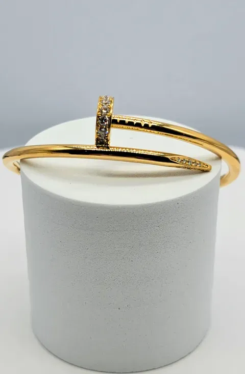 Gold bracelet with a rhinestone accent displayed on a white pedestal against a gray background
