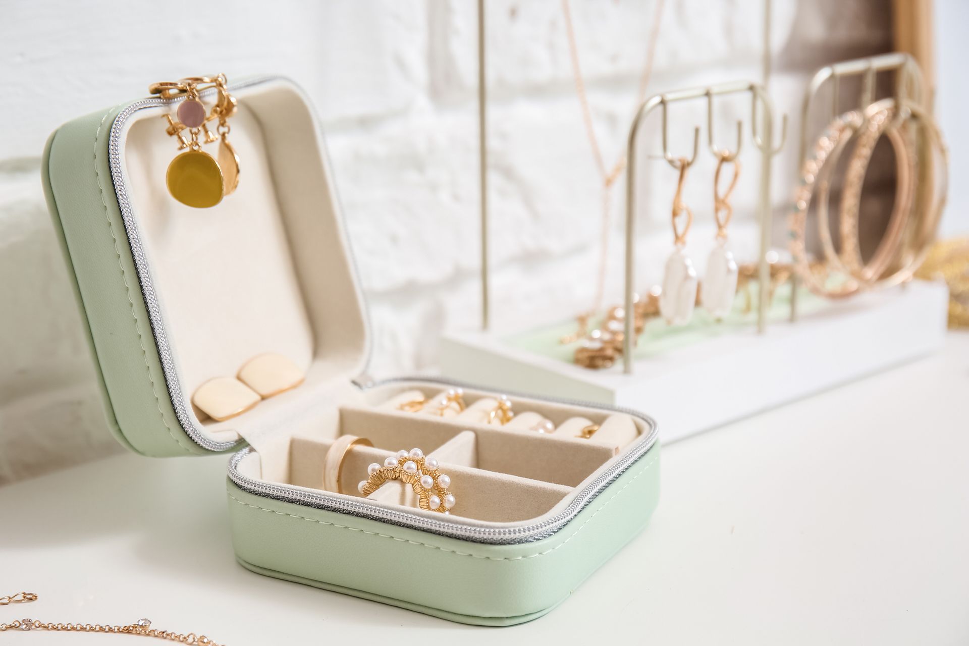 Mint jewelry box open with gold rings and earrings on a bright white vanity