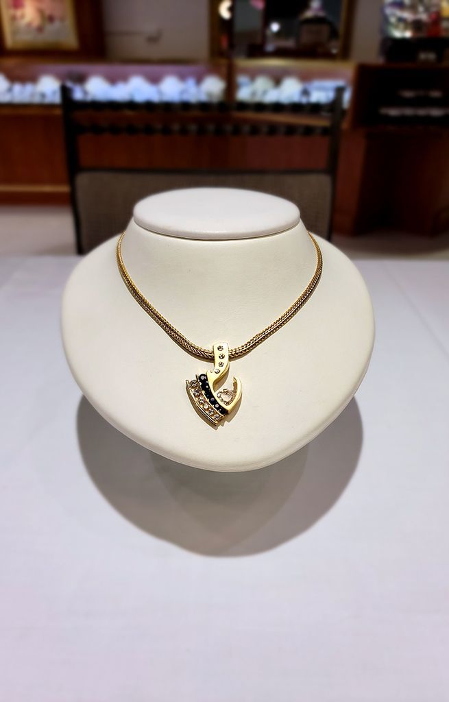 Gold necklace with a heart pendant displayed on a white jewelry stand in a store showcase