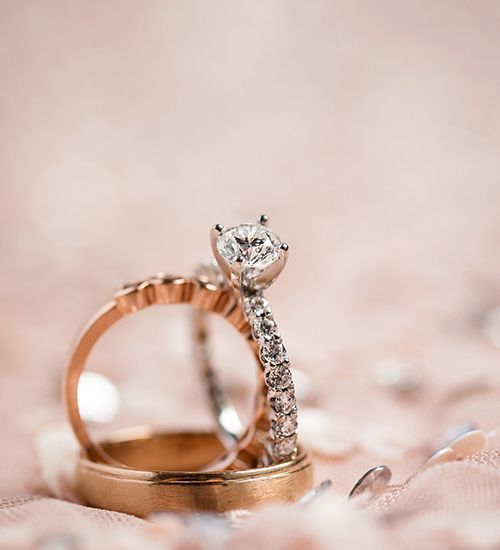 Two rose gold rings, one with a diamond, on a soft pink background with scattered petals
