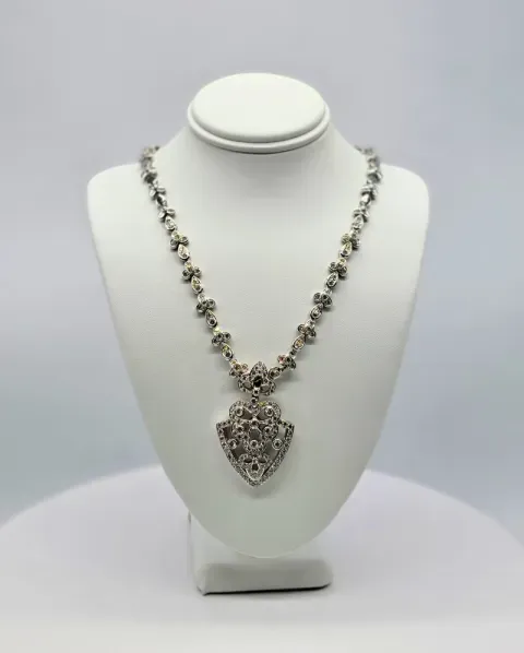 Silver necklace displayed on a white bust stand, featuring an ornate heart-shaped pendant.