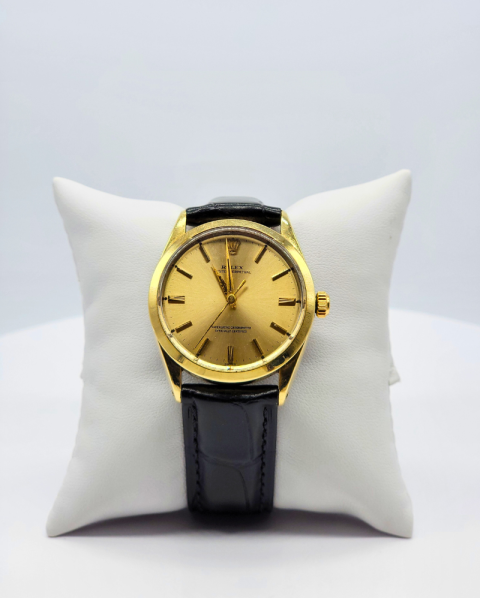 Gold wristwatch with black leather strap on a white display pillow