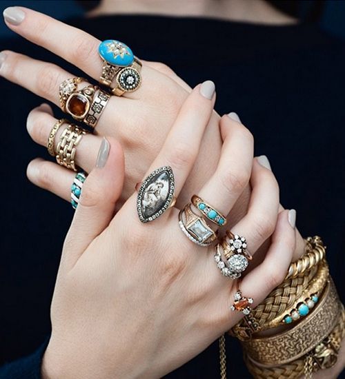 Hands with stacked rings and bracelets, including turquoise and gold jewelry, posed against a dark background