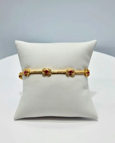Gold bracelet with red flower accents resting on a white display pillow