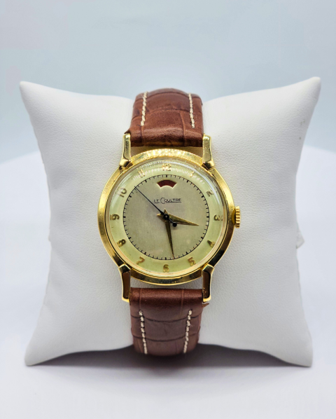 Gold wristwatch with brown leather strap on a white cushion