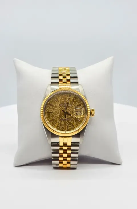 Gold-tone wristwatch with a silver-and-gold band on a white cushion