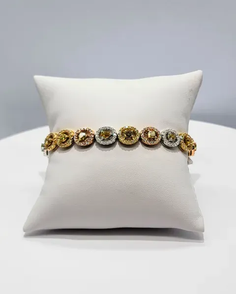 Gold bracelet with round floral charms displayed on a white cushion