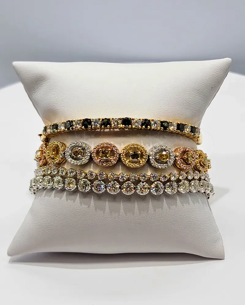 White cushion displaying three ornate gold and silver beaded bracelets on a plain gray background