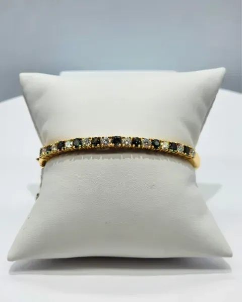 White cushion displaying a gold bracelet with black and clear stones, centered against a light background