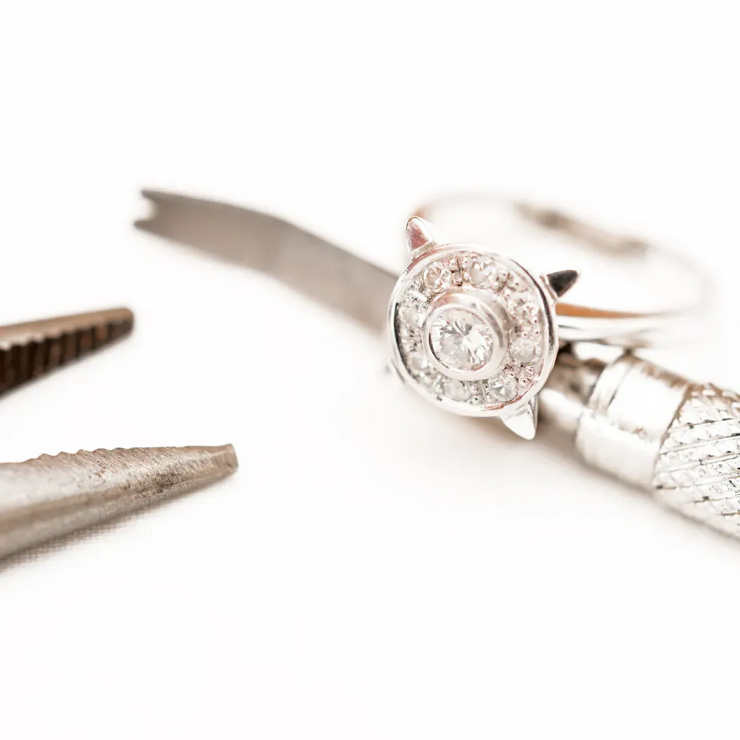 Diamond ring next to tweezers on a white background