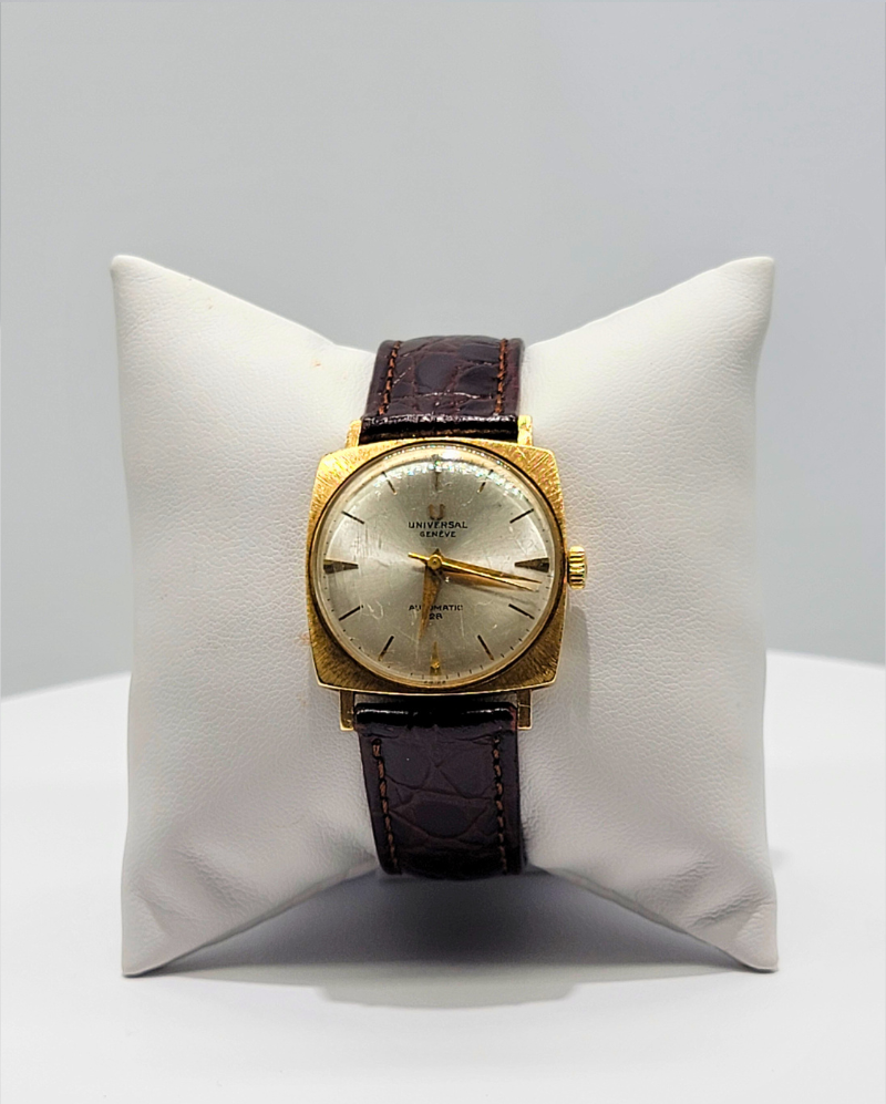 Gold wristwatch with brown leather strap displayed on a white cushion