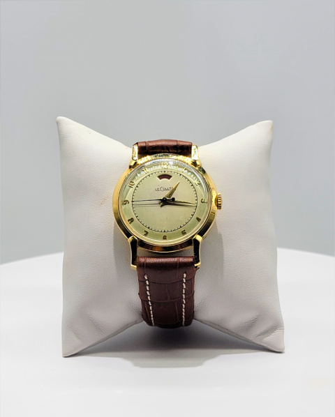 Gold wristwatch with brown leather strap displayed on a white cushion.
