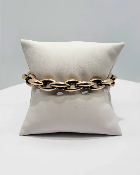 White pillow with a chunky gold chain wrapped around its middle on a plain gray background
