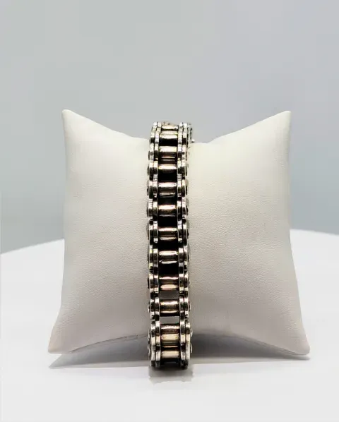 Silver and black bracelet centered on a white display cushion against a gray background