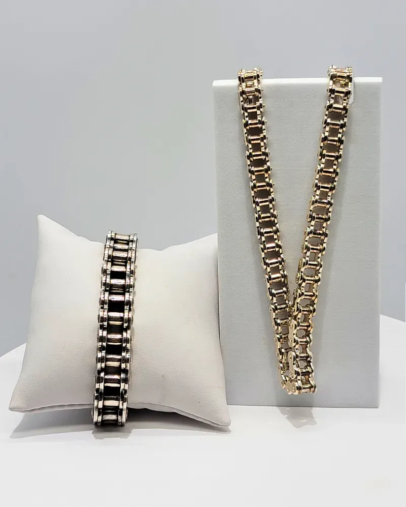 Two gold-tone chain bracelets displayed on a white cushion and stand