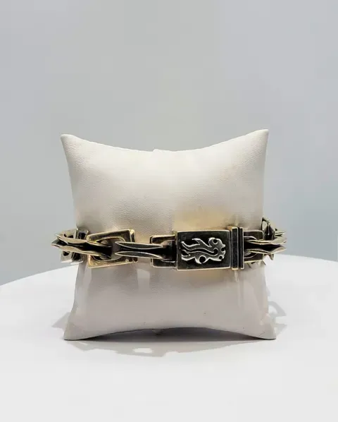 Gold-and-black chain bracelet wrapped around a cream cushion on a white surface.