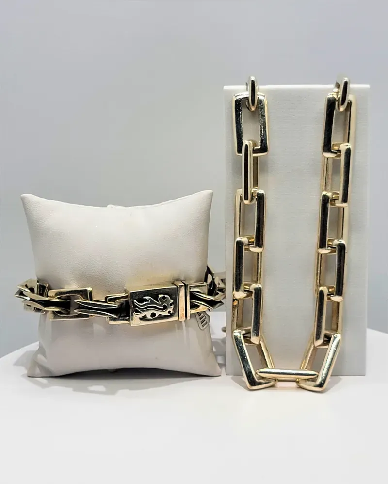 Gold-and-black chain necklace displayed on a white pillow beside a standing panel on a white background