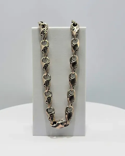 Silver heart-link necklace displayed on a white stand against a gray background