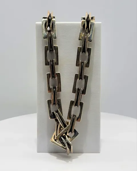 Gold and silver chain necklace draped over a white display block