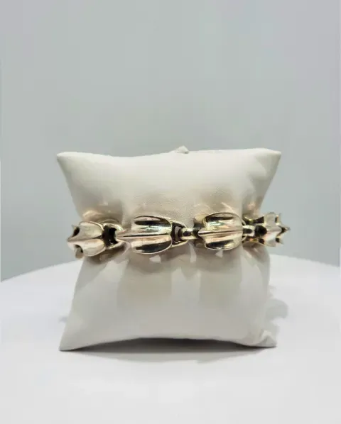 Gold chain bracelet displayed on a white pillow against a light gray background