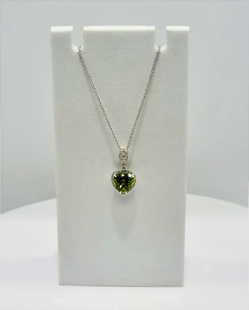 Silver necklace with a green heart-shaped pendant on a white display stand