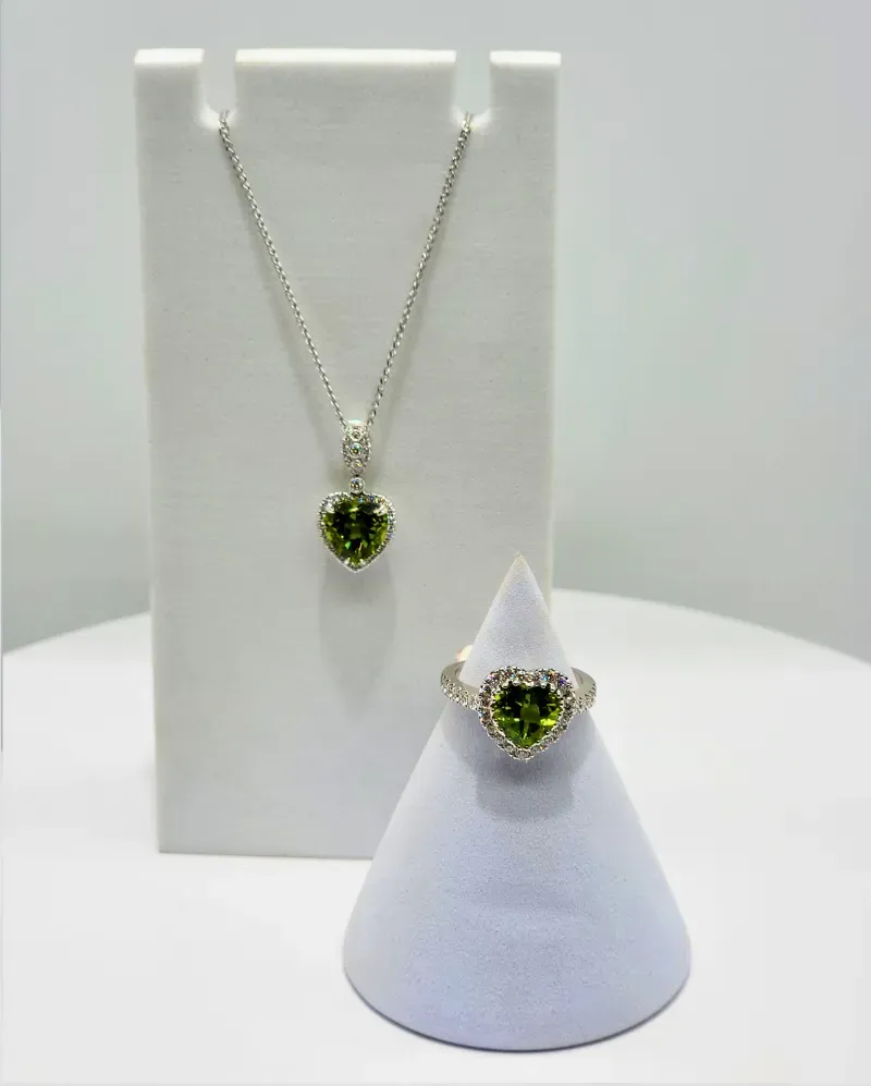 Silver necklace and matching ring with green gemstones displayed on white stands.