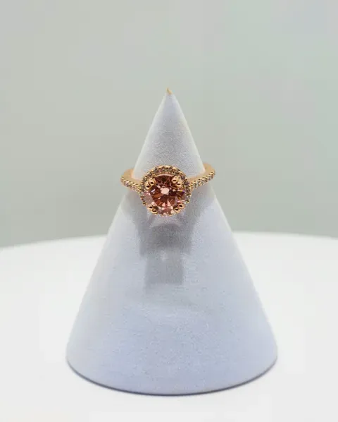Rose gold ring with a pink gemstone displayed on a white cone stand