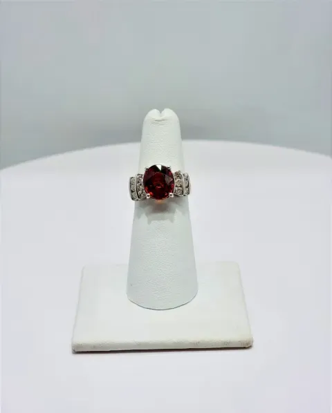Silver ring with a dark red gemstone displayed on a white stand