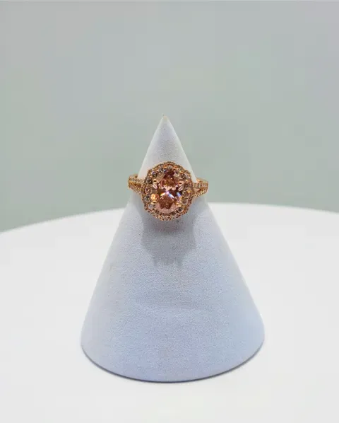 Gold ring with a pink gemstone displayed on a white cone stand against a light gray background