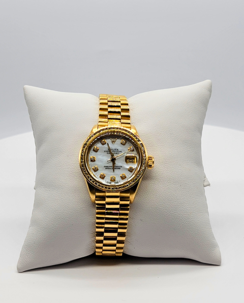 Gold wristwatch on a white cushion against a gray background