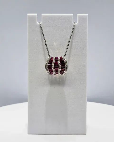 Silver necklace with a red striped pendant displayed on a white stand